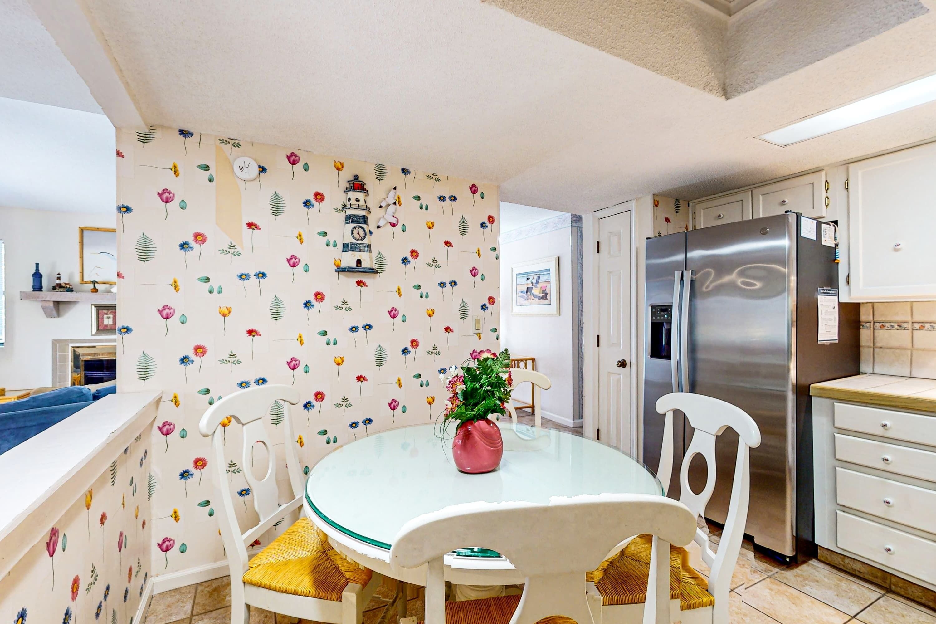 A kitchen with a round table, white chairs, a stainless steel refrigerator, and a floral-patterned wall.