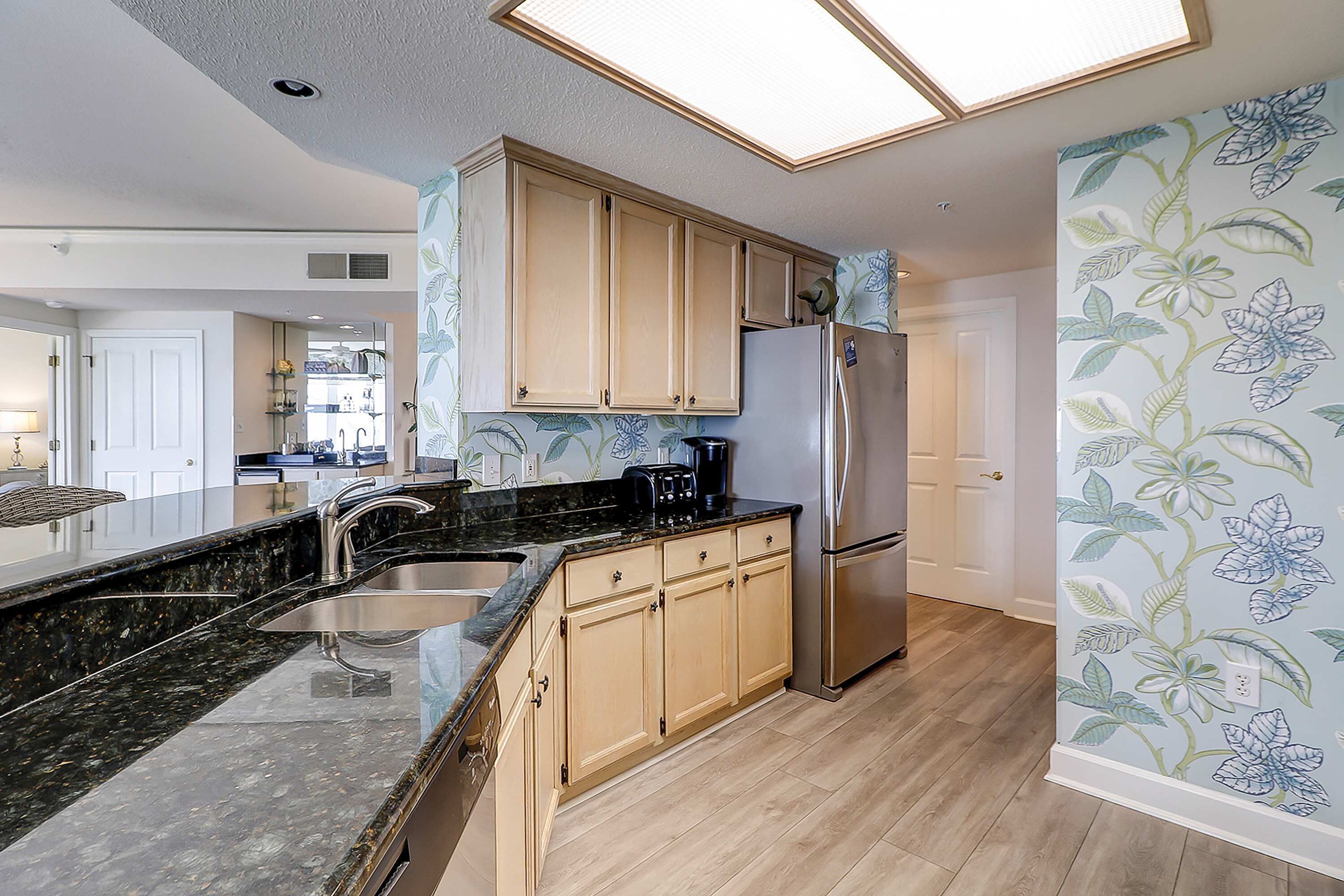 A modern kitchen with a granite countertop, stainless steel appliances, and light wood cabinetry.
