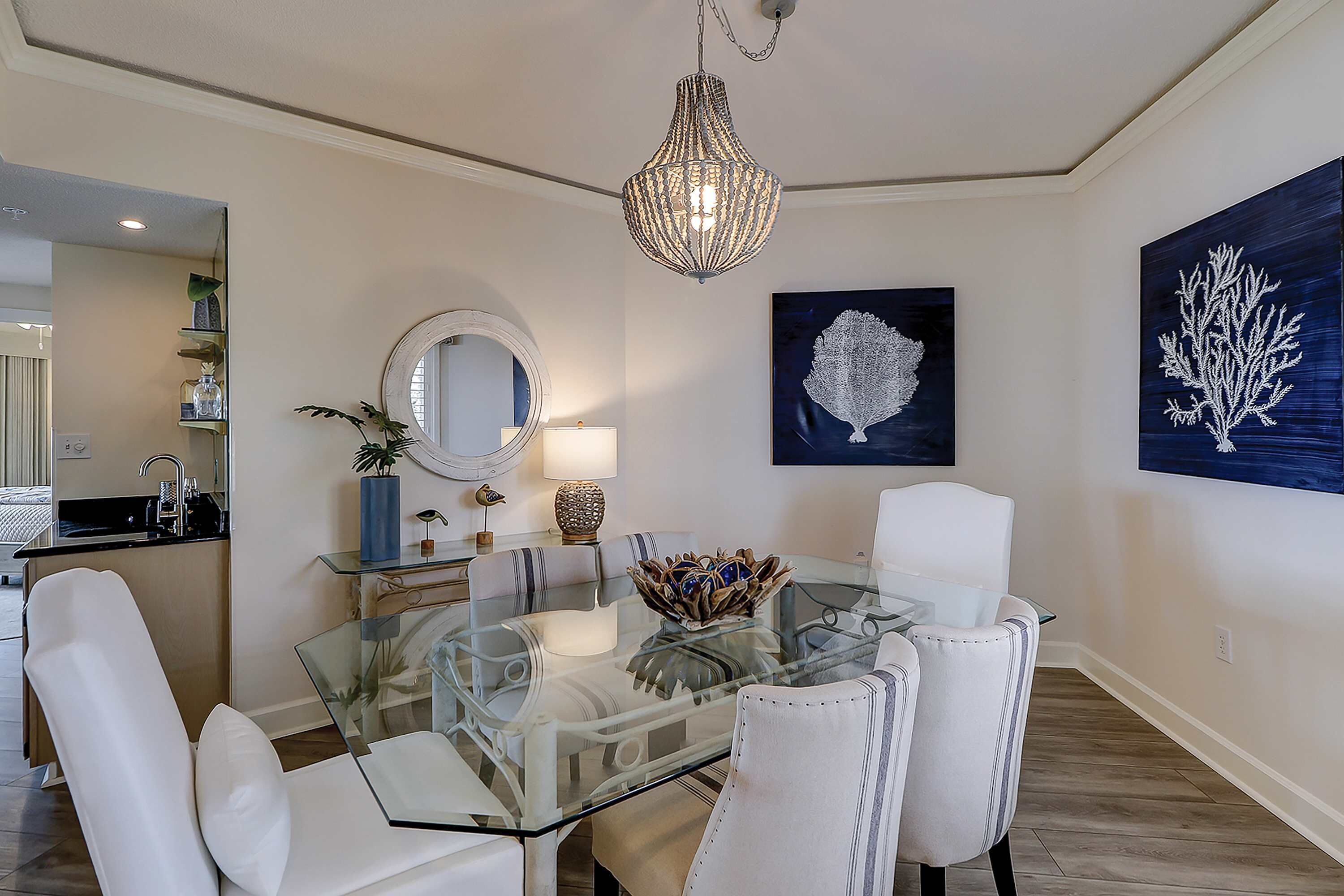 Comedor con mesa de vidrio, sillas blancas, candelabro y decoración en la pared.