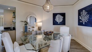 Un espace repas avec une table en verre, des chaises blanches, un lustre et des œuvres d’art murales.