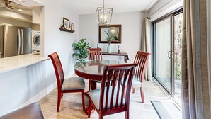 A dining area with a round table, wooden chairs, a chandelier, and a view through a glass door. - Roomy Villa with WiFi, Pool, & Hot Tub - Steps from the Ocean (Hilton Head)