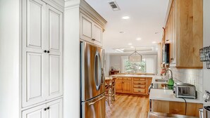 A kitchen with white cabinets, stainless steel appliances, wooden flooring, and a large window. - Delightful getaway with golf course views, private pool, and high-speed WiFi (Hilton Head)