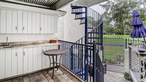 A covered outdoor area with a kitchen, a spiral staircase, and a view of a green landscape. - Delightful getaway with golf course views, private pool, and high-speed WiFi (Hilton Head)