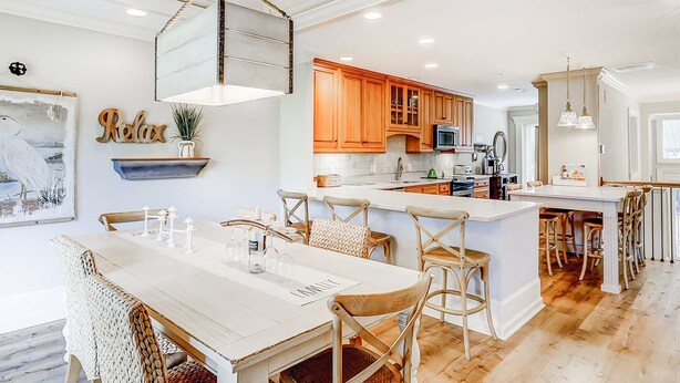 A modern kitchen with wooden cabinets, a central island with bar stools, and a dining area with a white table and chairs. - Delightful getaway with golf course views, private pool, and high-speed WiFi (Hilton Head)