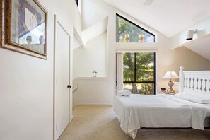 Ein Schlafzimmer mit Bett, Fenster, einem gerahmten Bild und einer Tür.