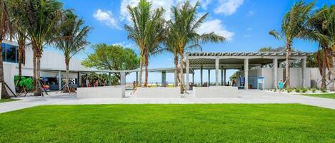 A modern building with a covered outdoor area, palm trees, and a well-maintained lawn.