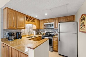 A kitchen with wooden cabinets, a granite countertop, a microwave, a refrigerator, and a coffee maker. - Coconut Cove: Perfect Location to Beach & Dining! (Sarasota)