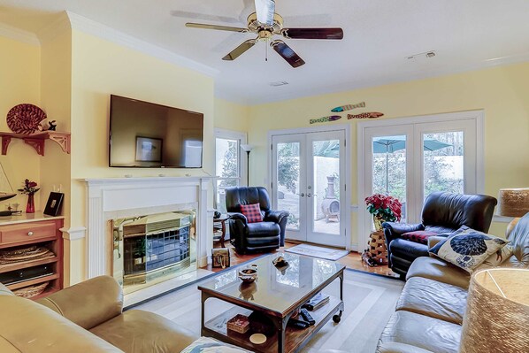 Un salon avec une cheminée, des fauteuils en cuir, une table basse et un ventilateur de plafond.
