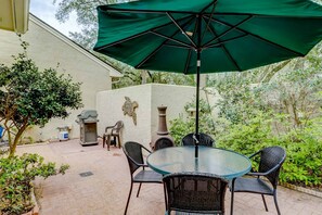 Une terrasse avec une table et des chaises en verre, un parasol vert et une cheminée en pierre.
