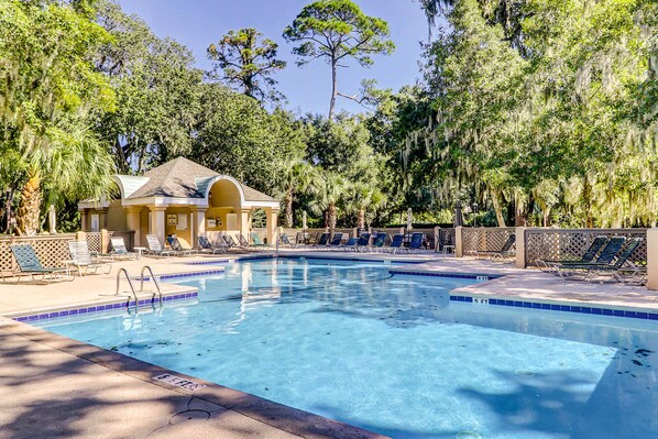 A swimming pool with lounge chairs, a covered seating area, and trees in the background. - Second Floor Condo with Free WiFi, Shared Pool, Hot Tub, Balcony, Golf Course View (Hilton Head)