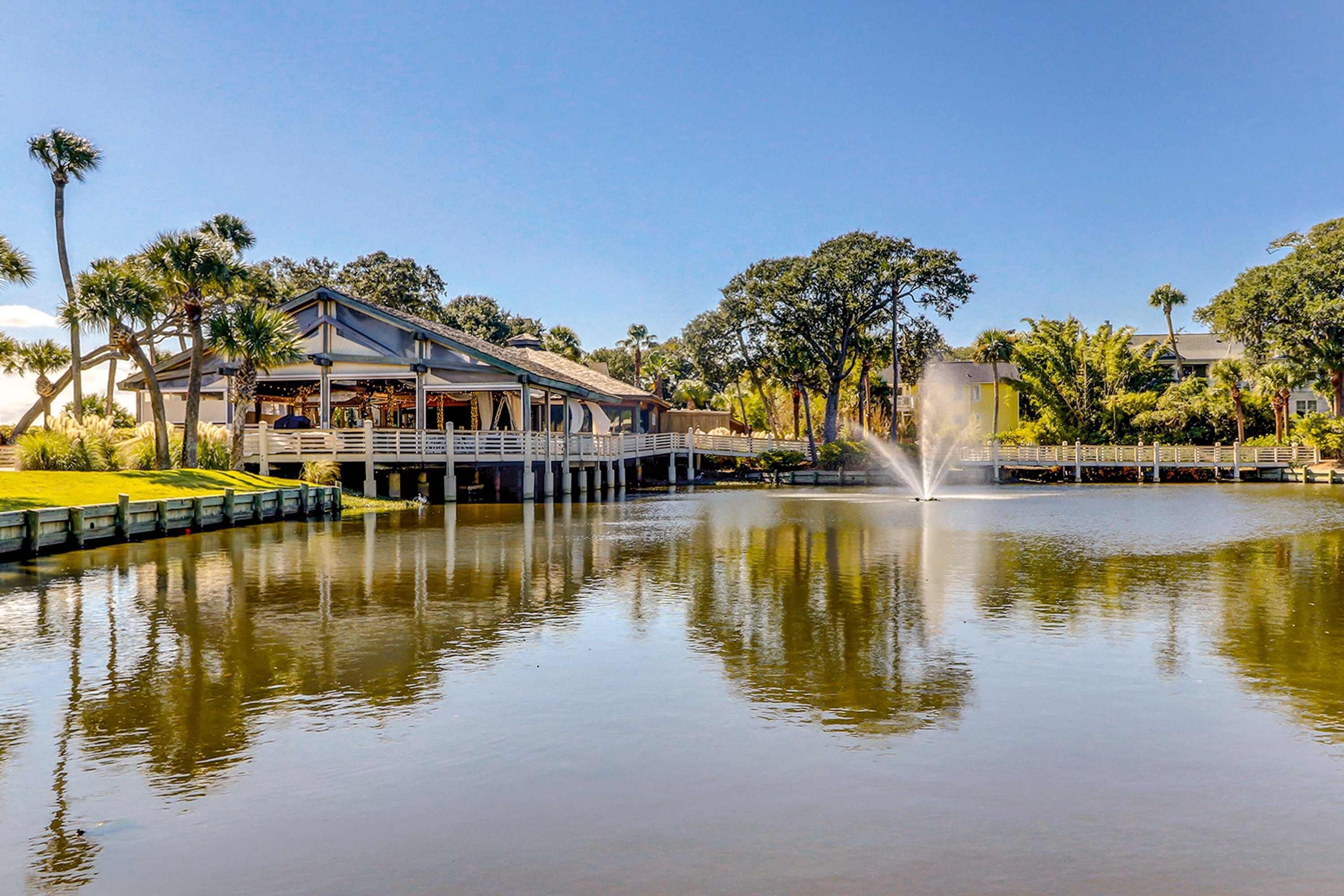 A waterfront hotel with a dock, a fountain, and lush greenery.