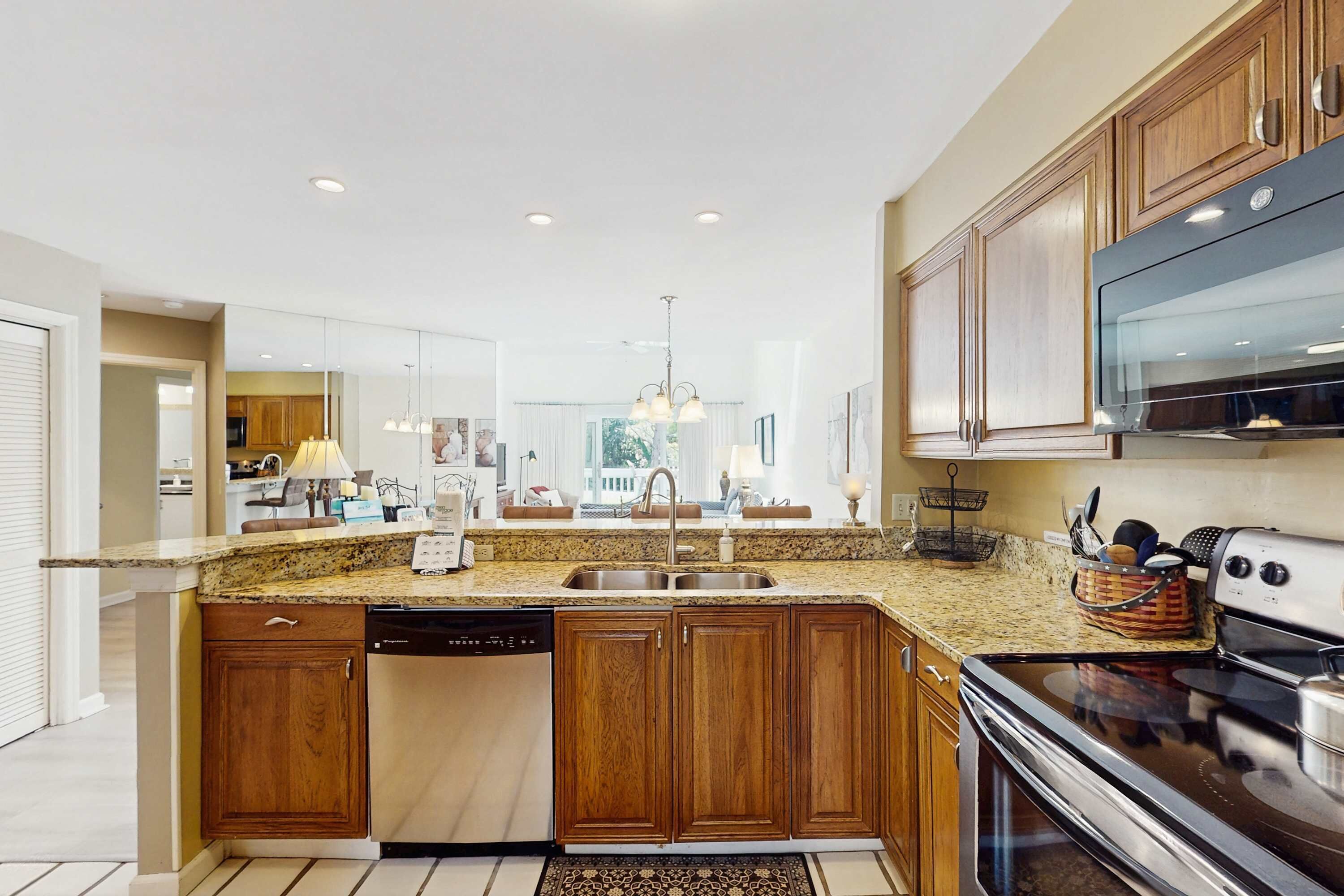 A modern kitchen with granite countertops, wooden cabinets, a built-in dishwasher, a stainless steel oven, and a large island with a sink.