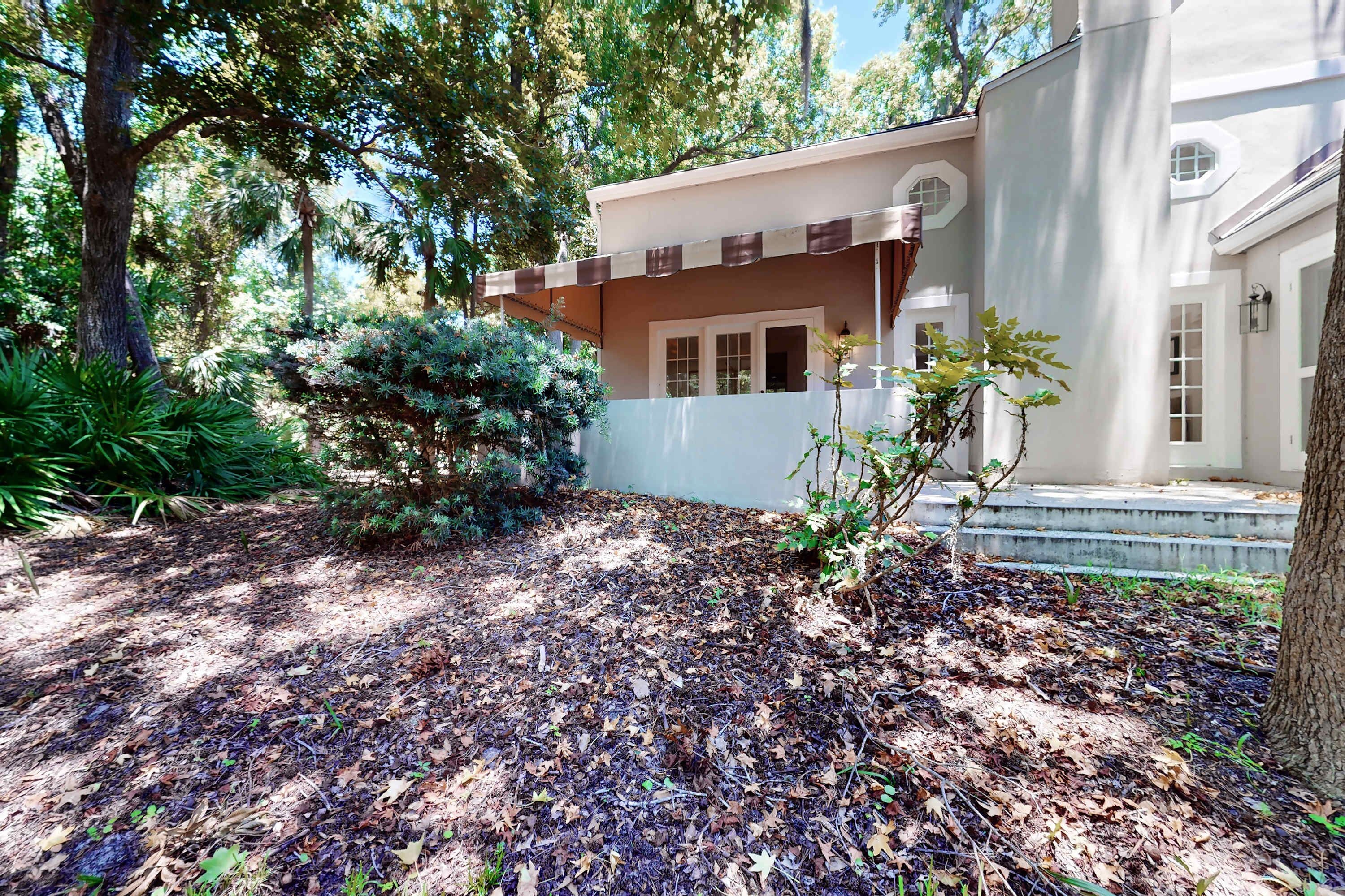 A house with a covered porch, a garden with trees and shrubs, and a white exterior wall.