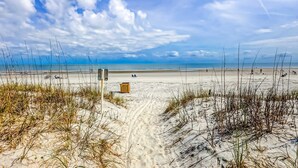Una spiaggia con un sentiero sabbioso che conduce all'acqua, un cestino e un cielo sereno.