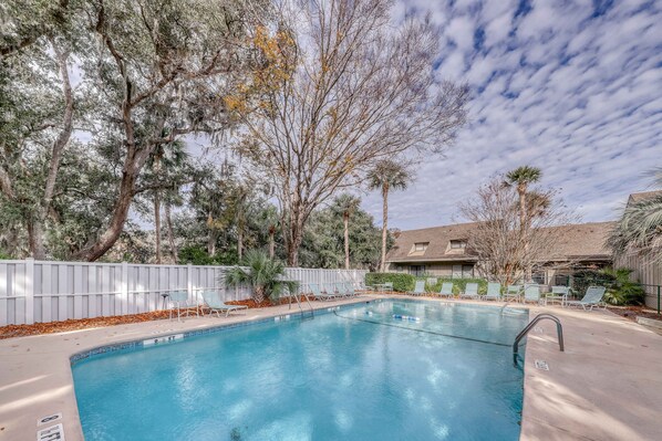 A swimming pool with lounge chairs, surrounded by trees and a fence. - Stylish Home with Private Deck, Shared Pool, and access to Dining and Shopping (Hilton Head)