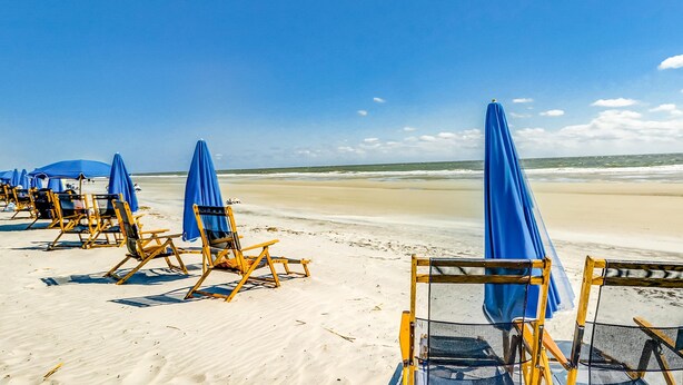 A beach with rows of sun loungers and umbrellas. - Island Bliss Near the Beach with Golf On Site, Shared Pool,Hot Tub & Private Deck (Hilton Head)