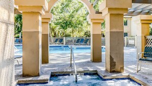 A pool area with a covered section, lounge chairs, and a view of trees. - Island Bliss Near the Beach with Golf On Site, Shared Pool,Hot Tub & Private Deck (Hilton Head)