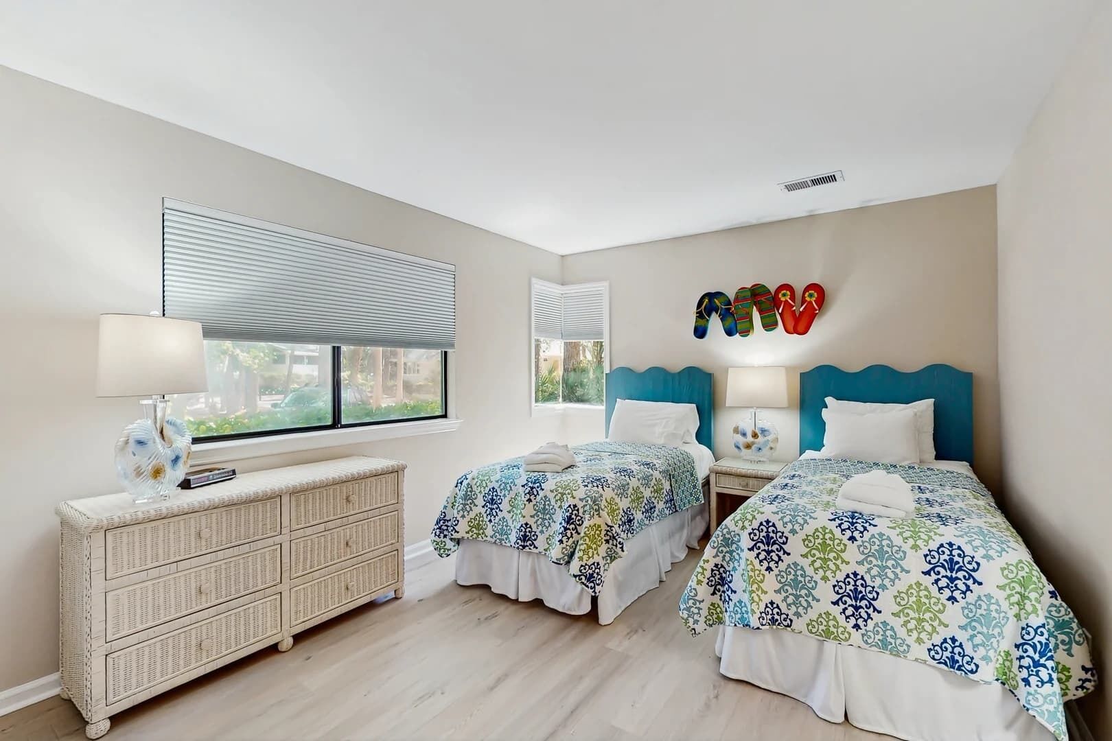 A bedroom with two beds, a dresser, and a window with blinds.