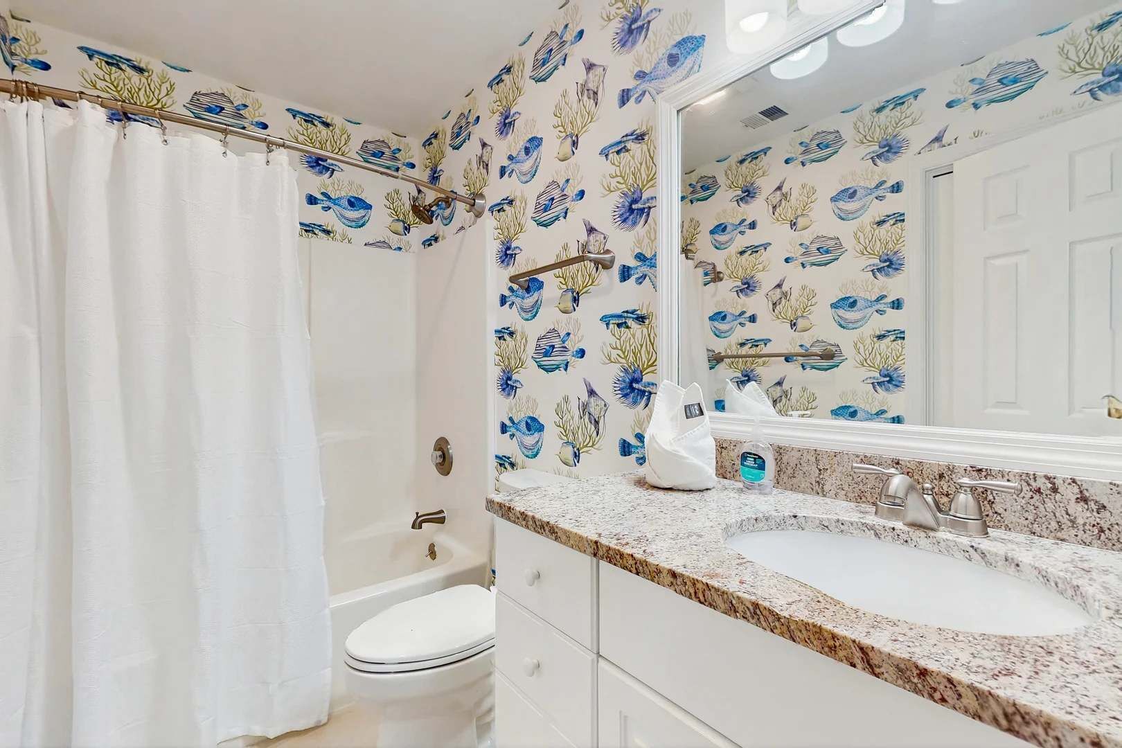 A bathroom with a white toilet, a sink with a marble countertop, and a shower curtain.