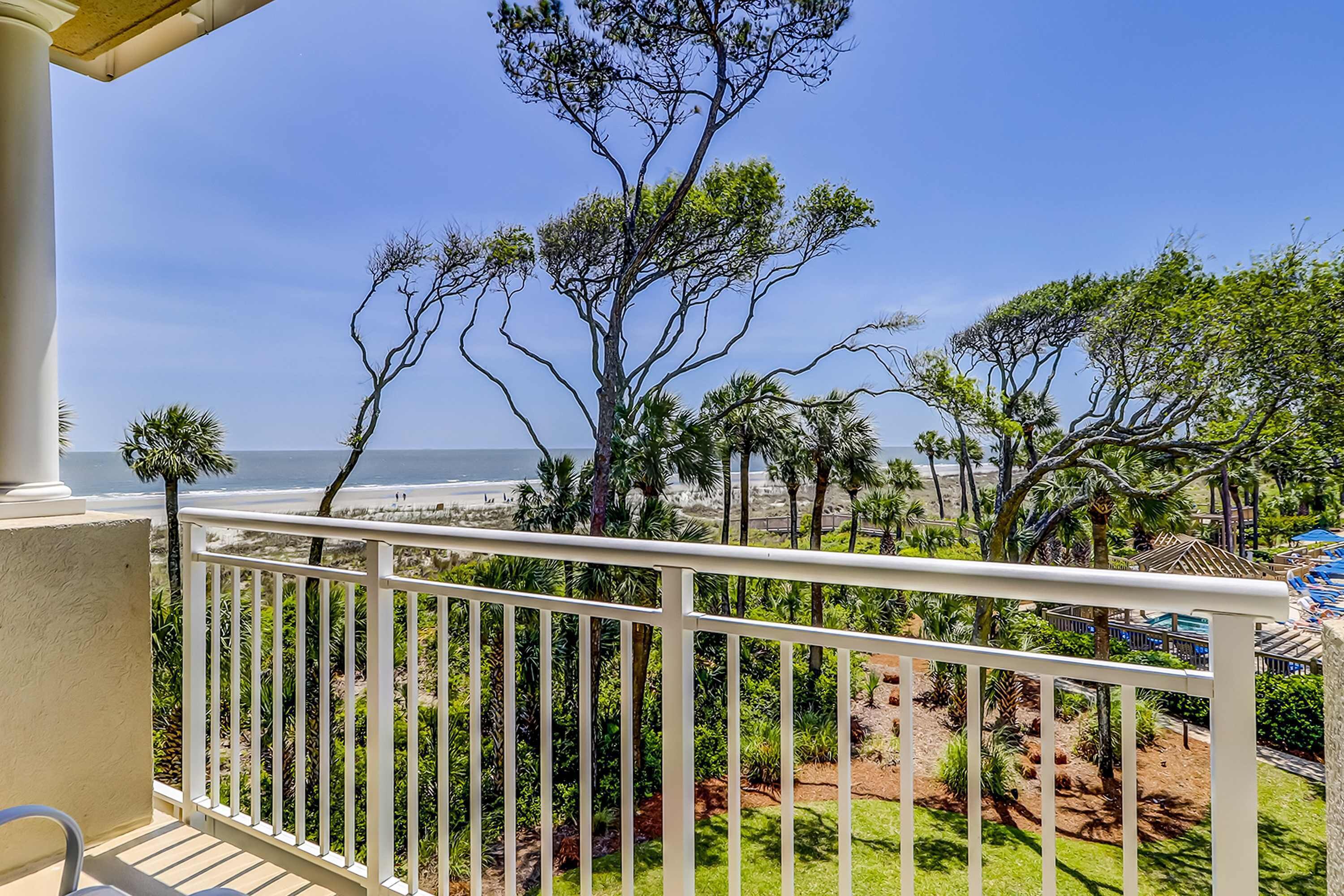 A balcony with a view of the beach, palm trees, and a clear sky.