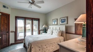 Um quarto com cama, um ventilador de teto, uma mesa de cabeceira, uma luminária, uma lareira e uma porta que dá para uma varanda.