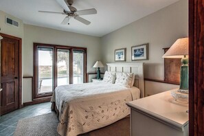 A bedroom with a bed, a ceiling fan, a nightstand, a lamp, a fireplace, and a door leading to a balcony. - Beachfront home with private pool, expansive deck & breathtaking views (Hilton Head)