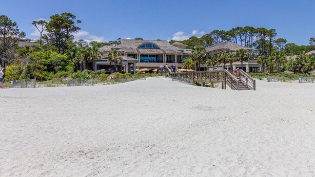 Une propriété située en bord de mer, comprenant un grand bâtiment, une plage de sable et un escalier en bois menant à l’entrée.