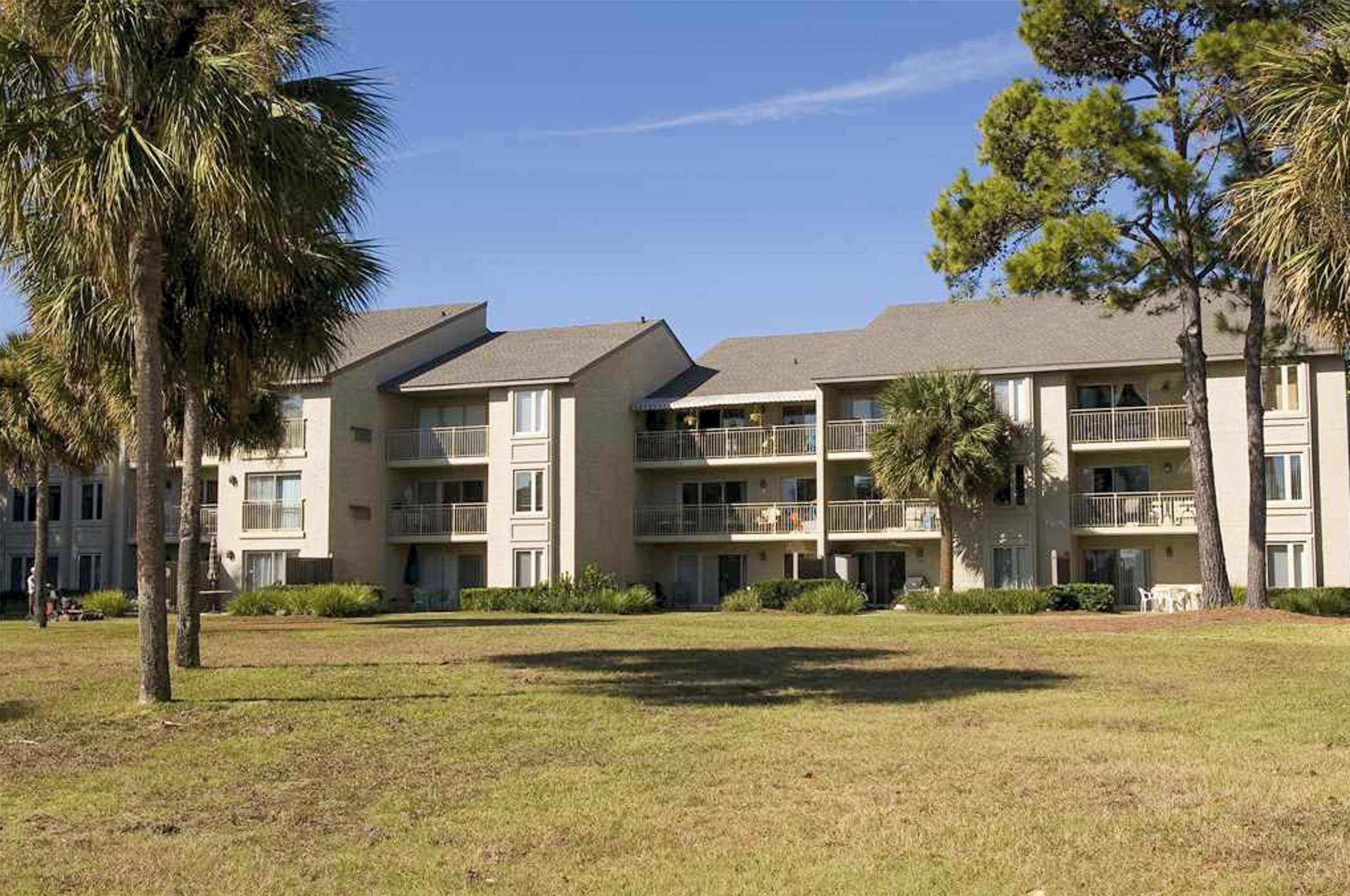 A multi-story hotel with balconies, a grassy courtyard, and palm trees.