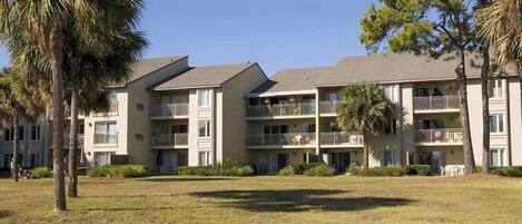 A multi-story hotel with balconies, a grassy courtyard, and palm trees.