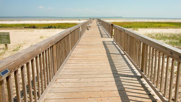 Ein hölzerner Steg führt zu einem Strand, ein Schild weist auf Parkordnung hin.