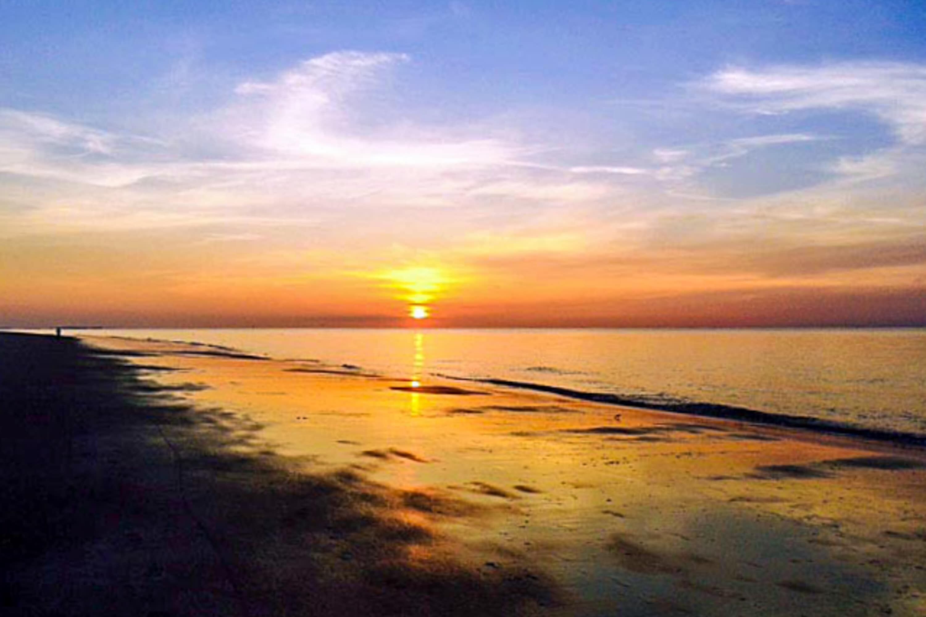A beach scene with a sunset, calm sea, and a distant horizon.