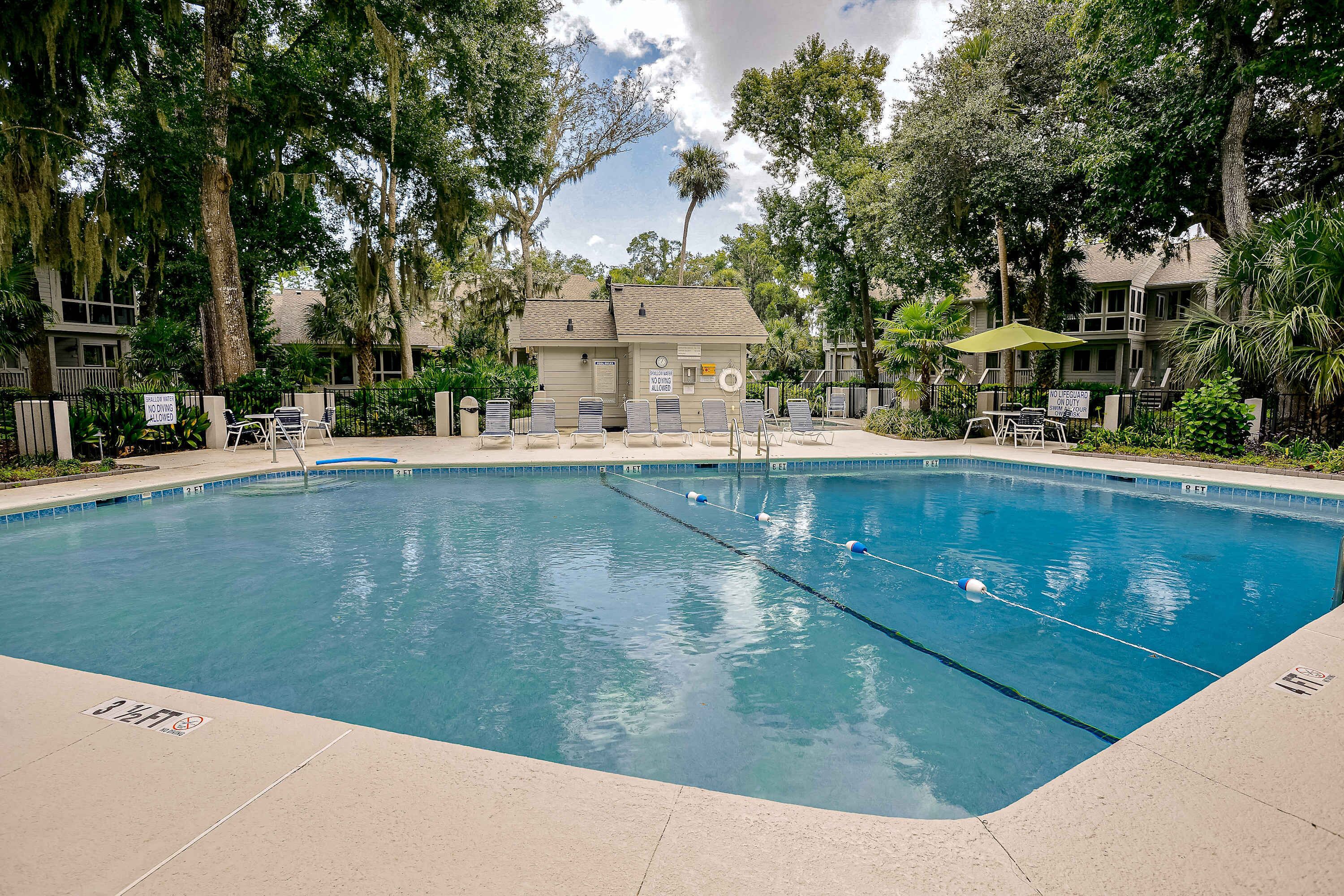 Una piscina con sillas de descanso, una torre de salvavidas y un edificio al fondo.