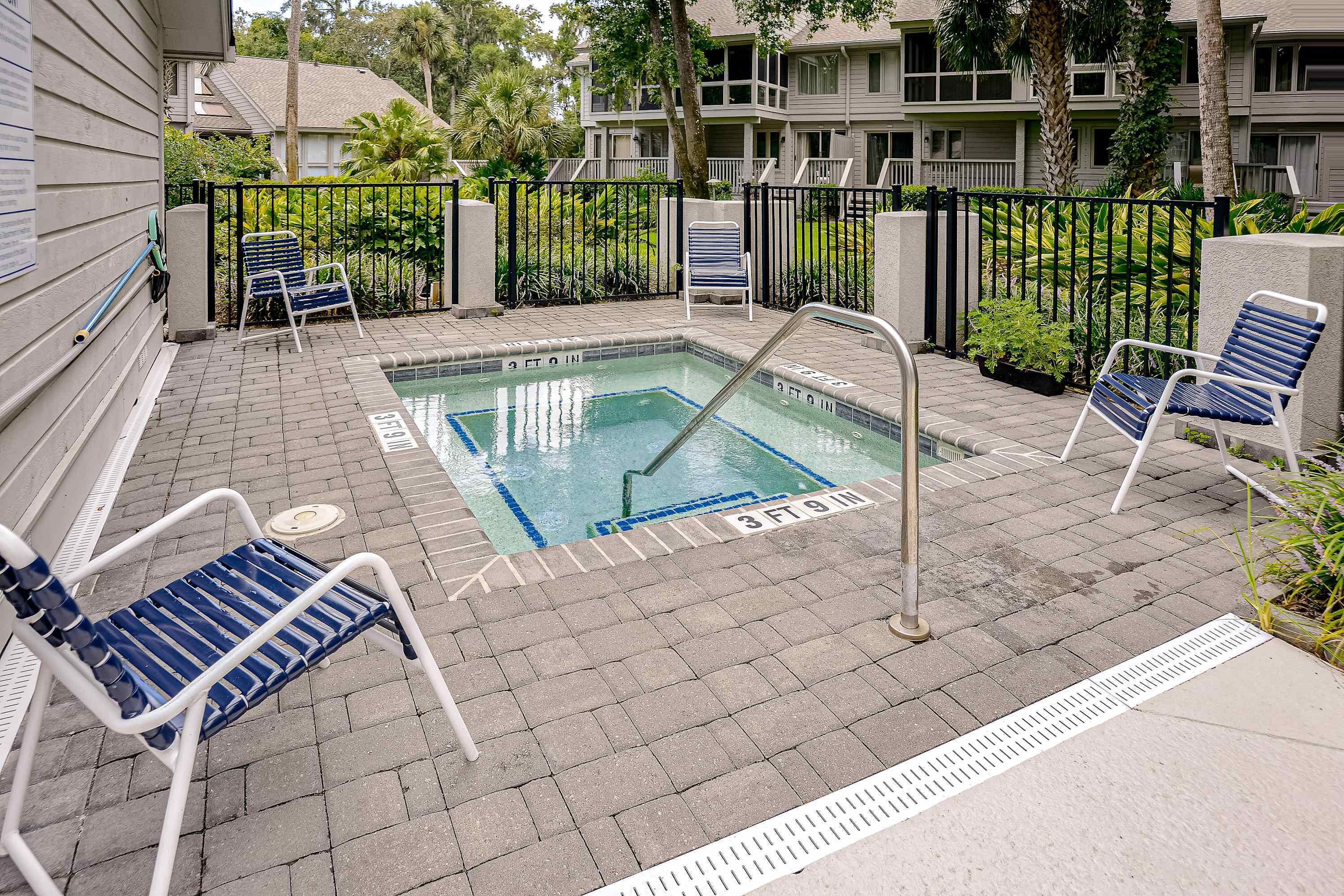 A pool area with a hot tub, lounge chairs, and a pool safety ladder.