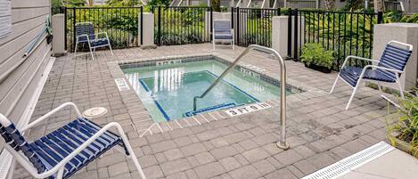 A pool area with a hot tub, lounge chairs, and a pool safety ladder.