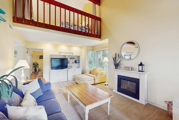 A living room with a sofa, coffee table, fireplace, television, and a staircase. - Villa with saltwater pool, golf, firepit, hot tub, & private beach access (Hilton Head)