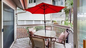 Une terrasse extérieure couverte, avec une table et des chaises, un parasol rouge et une clôture blanche.