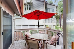 A covered outdoor patio with a table and chairs, a red umbrella, and a white fence. - Villa with saltwater pool, golf, firepit, hot tub, & private beach access (Hilton Head)