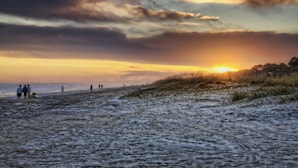 Een strand met mensen, duinen en een zonsondergang.