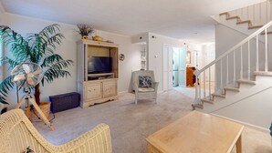 Ein Wohnzimmer mit Fernseher, Korbmöbeln, einem Ventilator und einer Treppe.