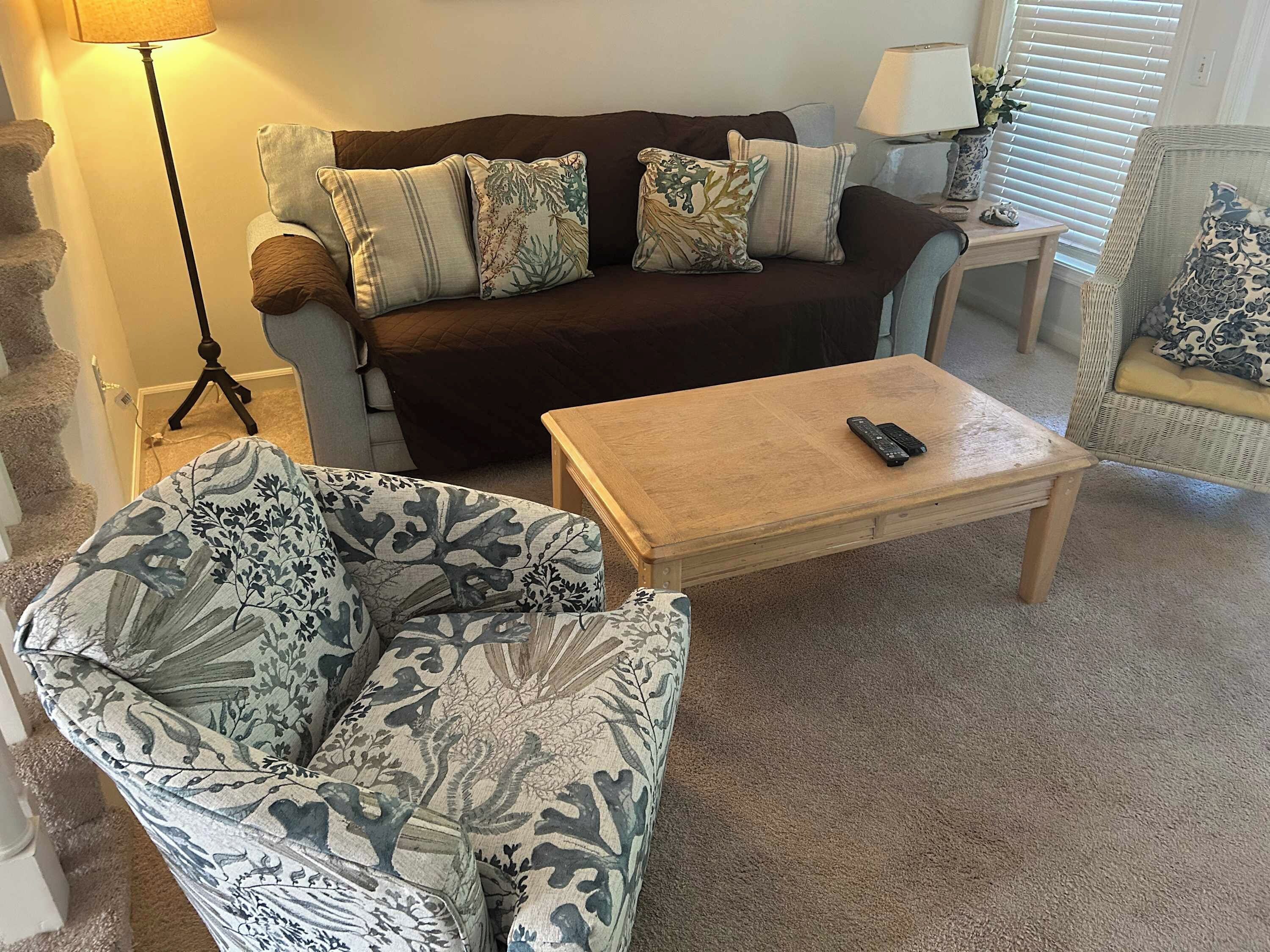 Un salon avec un canapé, un fauteuil à motifs, une table basse et une lampe.
