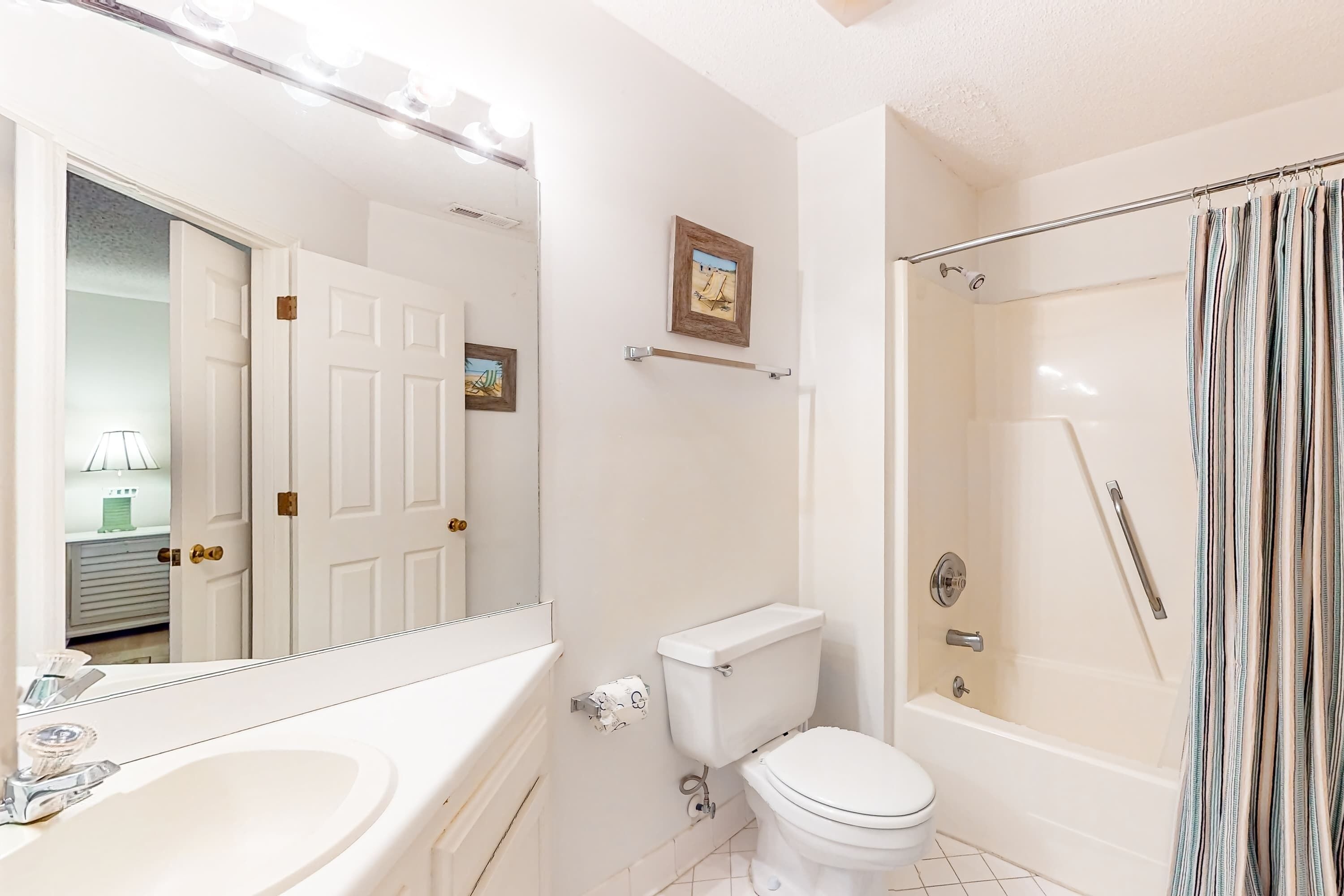A bathroom with a sink, toilet, shower, and a mirror.