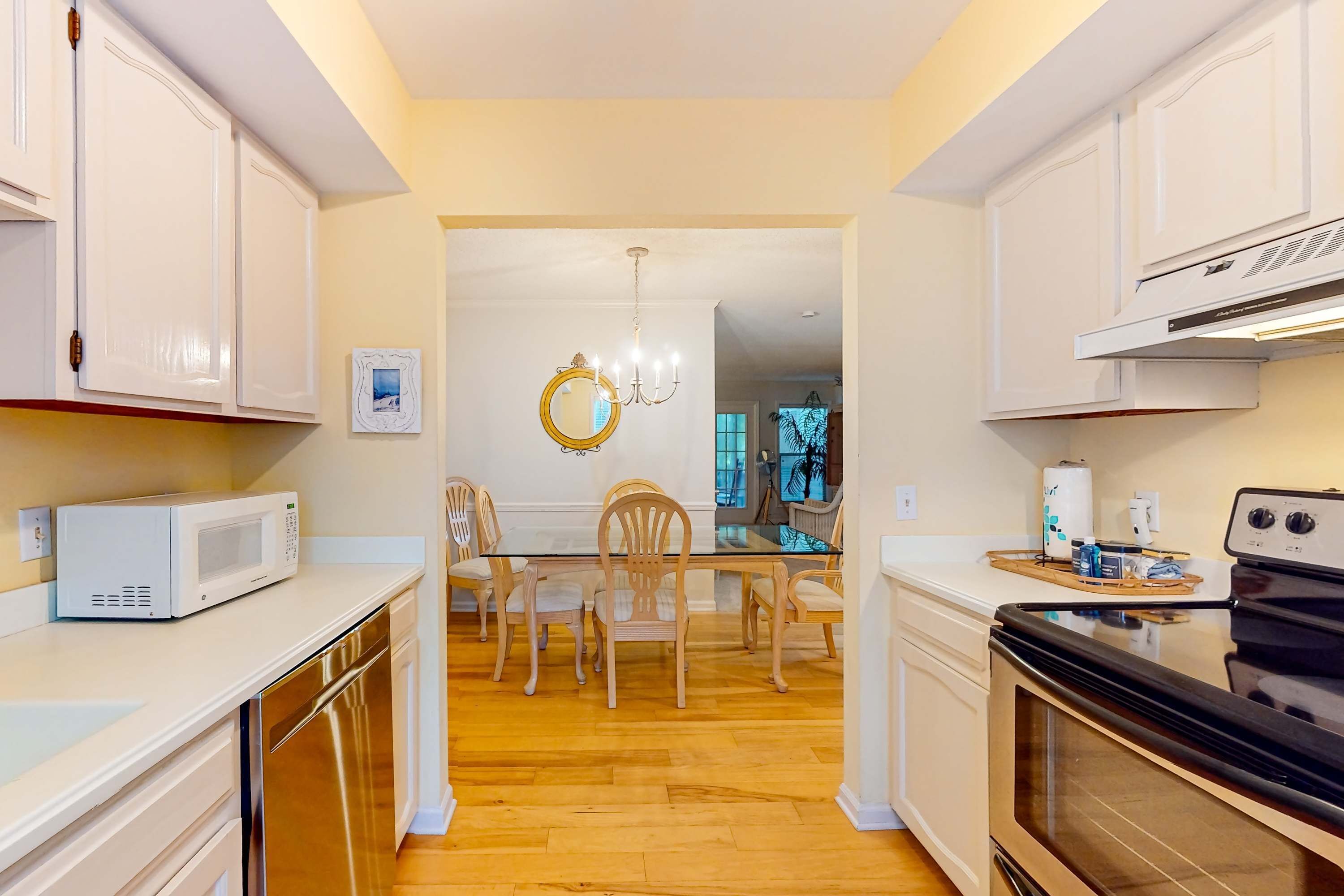 A kitchen with white cabinets, a microwave, a dishwasher, a dining table with chairs, a chandelier, and an oven.