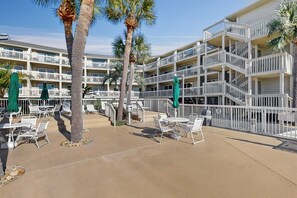 A hotel with outdoor seating, palm trees, and a multi-story building with balconies. - Beach condo with Ocean Views, outdoor pool & balcony - Walk to Beach (Hilton Head)