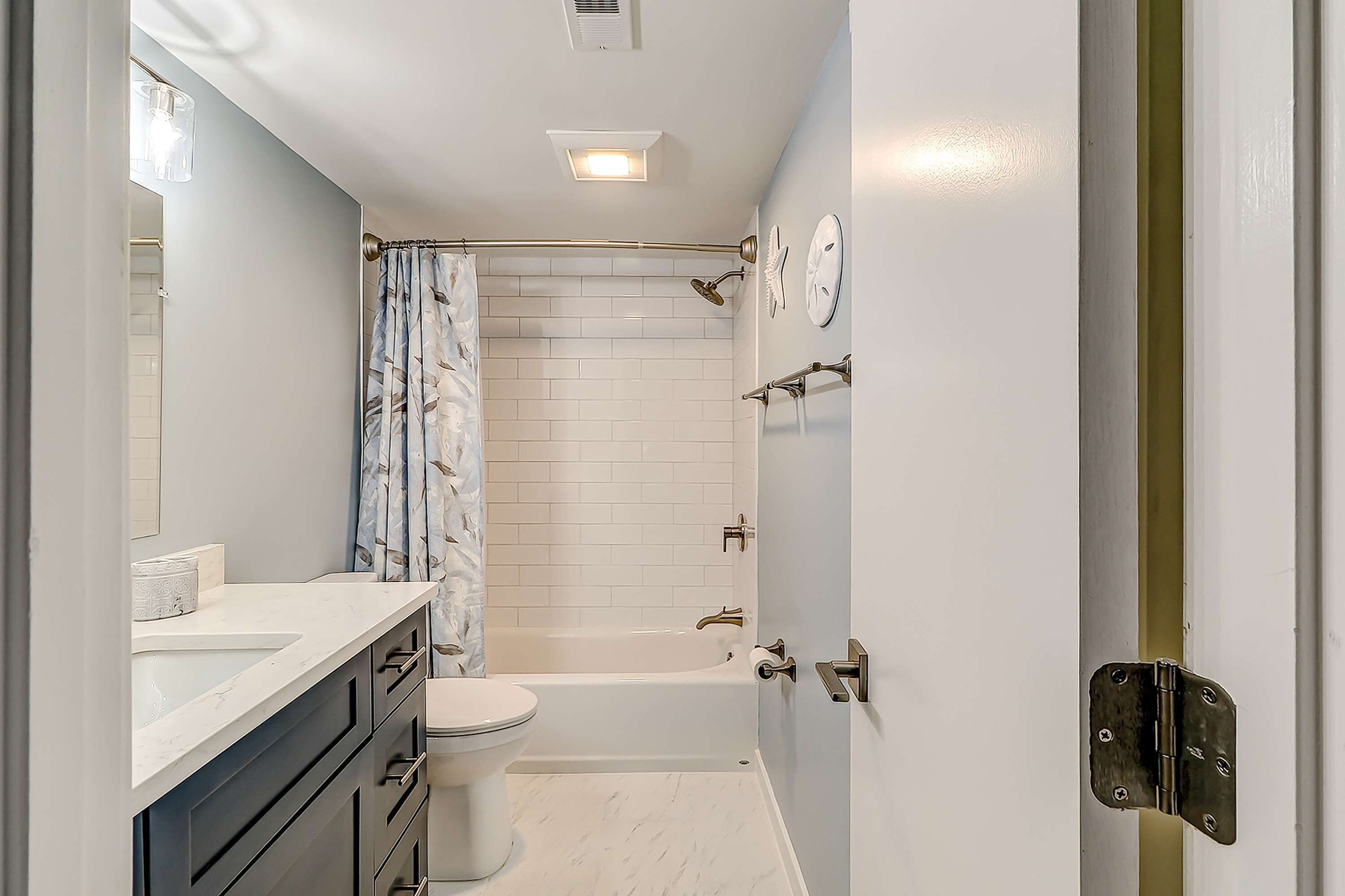 A bathroom with a toilet, sink, bathtub, shower curtain, and a mirror.