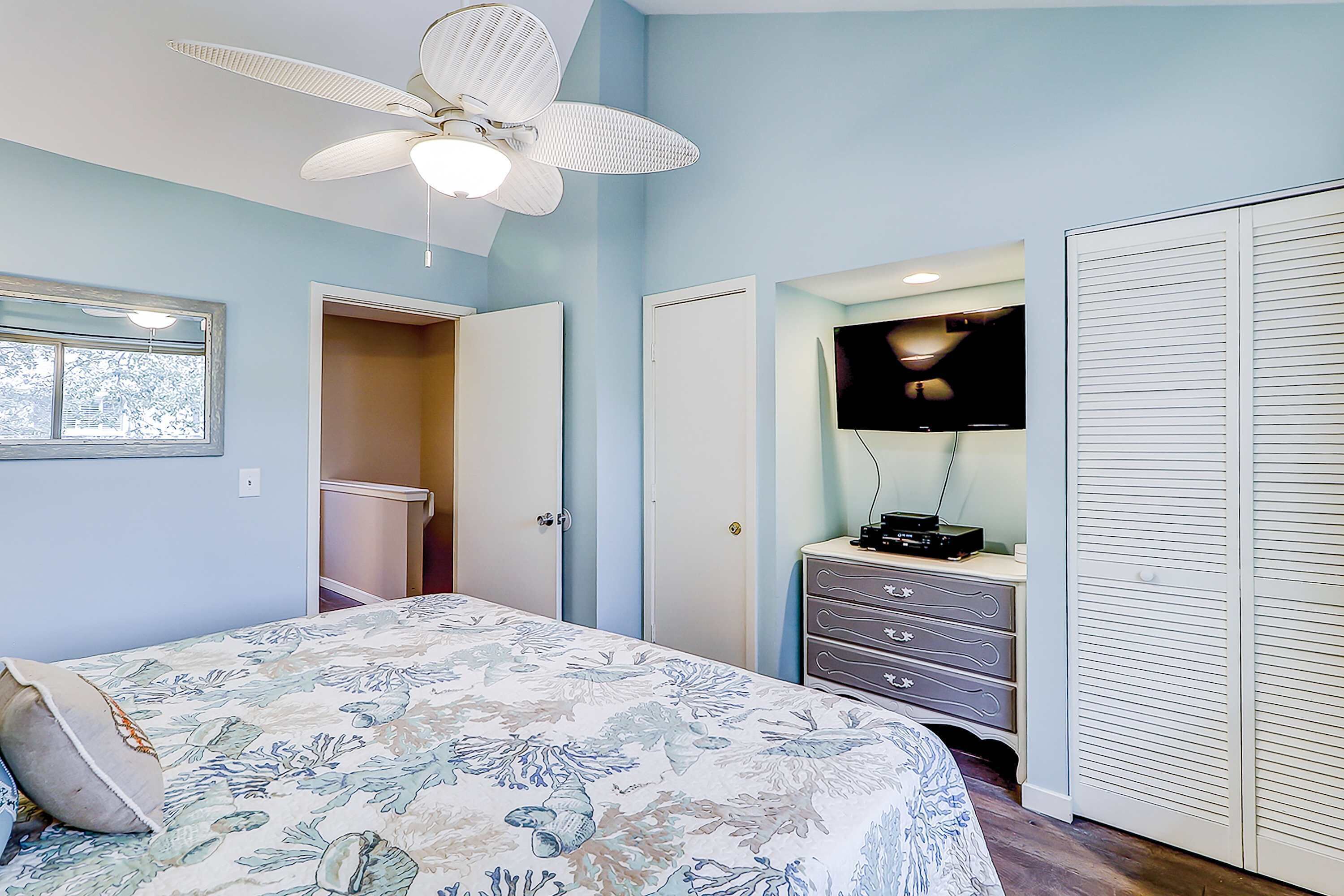 Ein Schlafzimmer mit Bett, Deckenventilator, Kommode, Fernseher und Kleiderschrank.