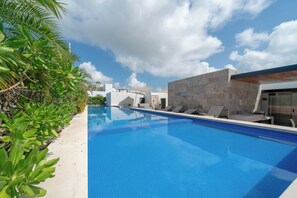 A swimming pool with lounge chairs, a stone wall, and tropical plants. - 2 Bedroom Condo - Rooftop Pool Opal 405 (Playa del Carmen)