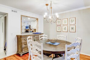 A dining room with a wooden table, white chairs, a chandelier, and framed botanical prints on the wall. - Pool View Villa Walking distance to Coligny Beach and Shops (Hilton Head)