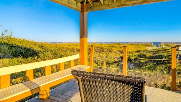 Eine Holzterrasse mit einem Korbstuhl, mit Blick auf eine Küstenlandschaft.