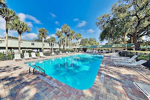 A swimming pool with lounge chairs, palm trees, and a brick patio.
