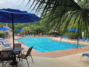 Une piscine bordée de parasols bleus, de chaises longues et d’une table avec des chaises.